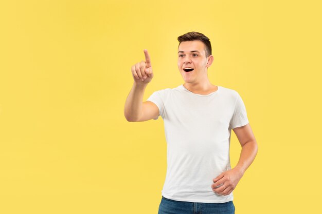 Halblanges Porträt des kaukasischen jungen Mannes auf gelbem Studiohintergrund. Schönes männliches Modell im Hemd. Konzept der menschlichen Emotionen, Gesichtsausdruck, Verkauf, Anzeige. Berühren einer leeren Suchleiste.