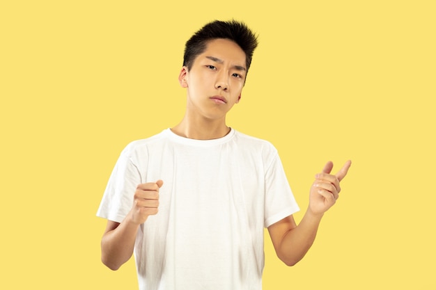 Halblanges Porträt des koreanischen jungen Mannes auf gelbem Studiohintergrund. Männliches Modell im weißen Hemd. Halten und einladen. Konzept menschlicher Emotionen, Gesichtsausdruck. Vorderansicht. Trendige Farben.