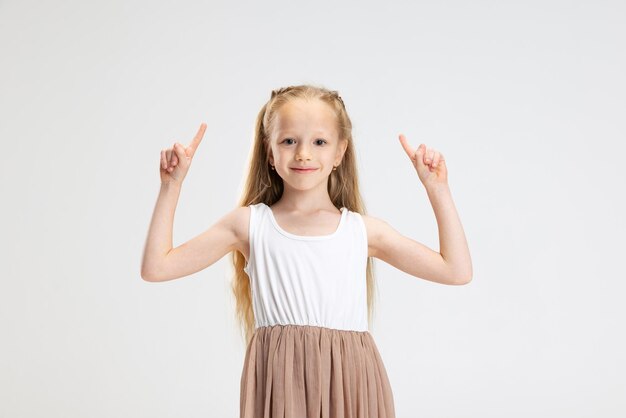 Halblanges Porträt eines niedlichen kleinen Mädchens in modernem, stilvollem Kleid, das isoliert auf weißem Studiohintergrund posiert Glückliches Kindheitskonzept