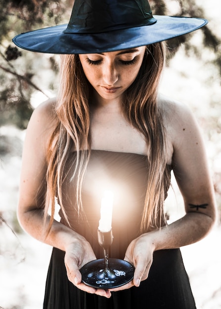 Kostenloses Foto halloween-hexe, die auf kerzenständer im sonnigen wald schaut