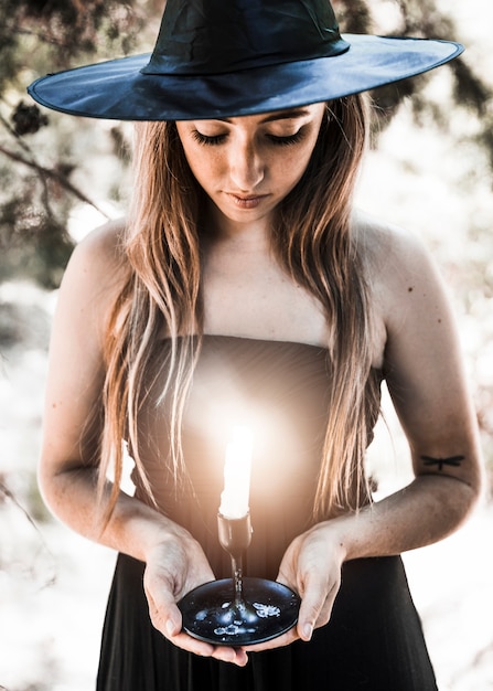 Halloween-Hexe, die auf Kerzenständer im sonnigen Wald schaut