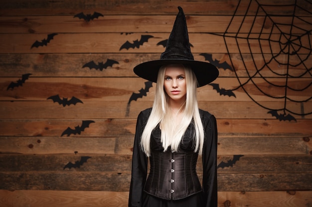 Halloween-Hexenkonzept glückliche Halloween-sexy Hexe, die über altem hölzernem Studiohintergrund posiert