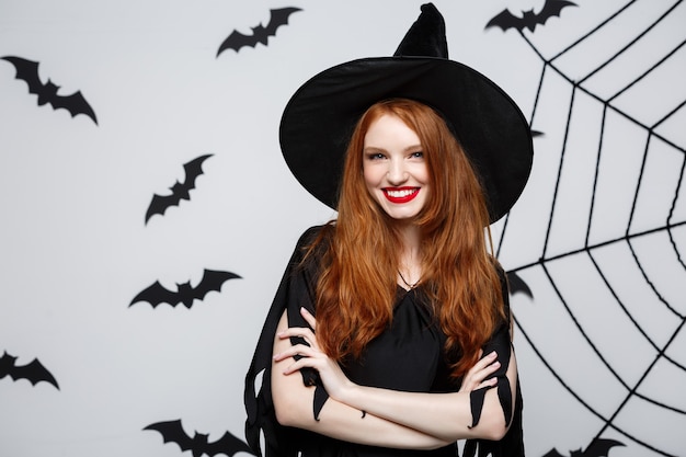 Halloween-konzept - schöne hexe, die hand hält und über grauer wand lächelt.