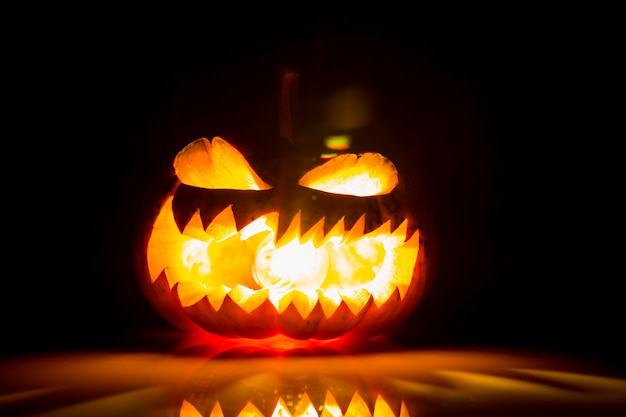 Halloween-Kürbis mit offenem Mund und mit Licht im Inneren und auf einem schwarzen Hintergrund