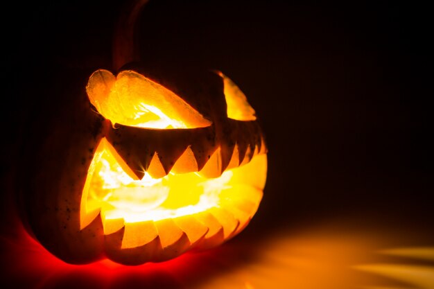 Halloween-Kürbis mit offenem Mund und mit Licht im Inneren und auf einem schwarzen Hintergrund