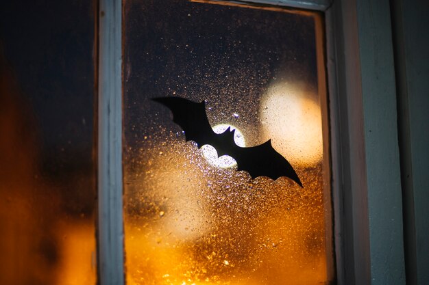 Halloween-Papierfledermaus, die das Fenster bedeckt mit Regentropfen verziert