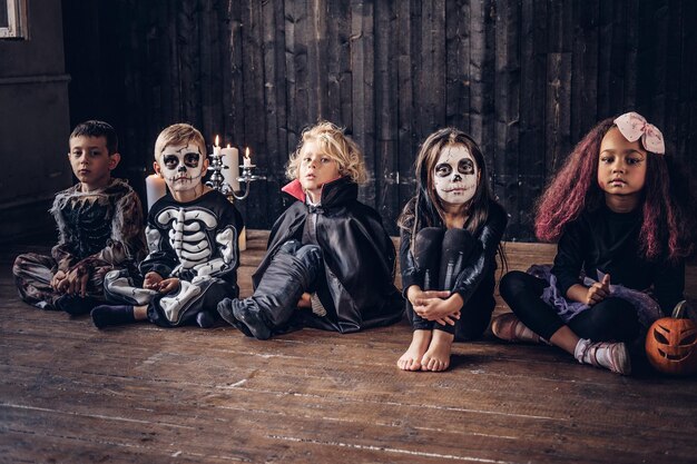 Halloween-Party mit Gruppenkindern, die zusammen auf einem Holzboden in einem alten Haus sitzen.