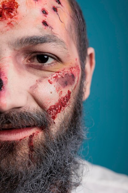 Halloween-Zombie mit blutigen Wunden und Narben auf der Hälfte des Gesichts, sieht aggressiv und böse vor der Studiokamera aus. Gefährliches, verwundetes, gehirnfressendes Monster, das beängstigend wirkt. Nahansicht.