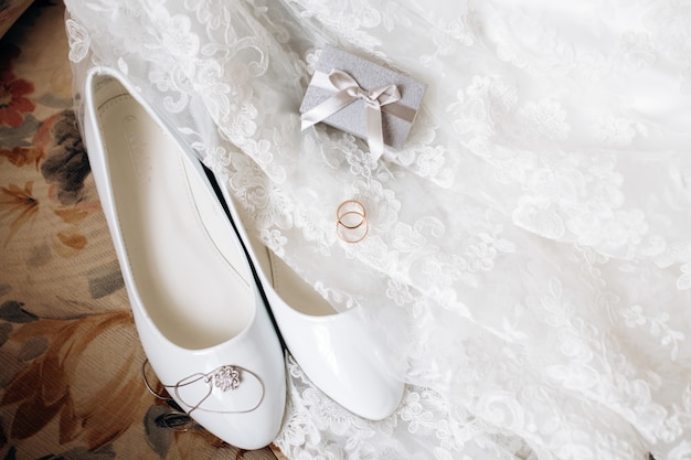 Halskette, weiße Schuhe und Eheringe auf dem Hochzeitskleid