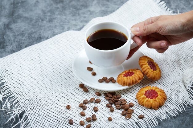 Halten Sie eine Tasse Kaffee mit Keksen und Kaffeebohnen.
