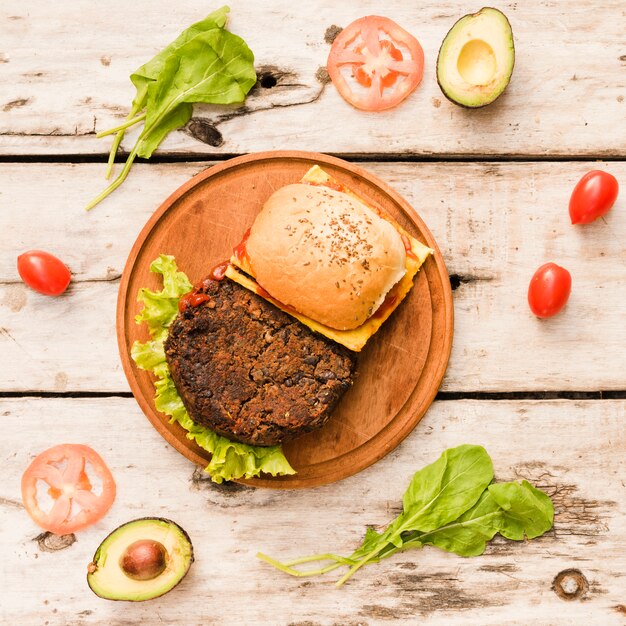 Hamburger mit Kopfsalat und Käse auf kreisförmigem hölzernem Brett auf Tabelle