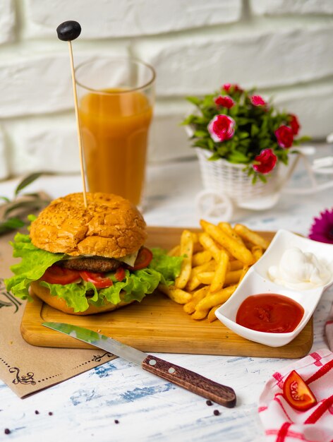 Hamburger mit Pommes-Frites auf hölzernem Brett mit Ketschup und Majonäse, Küche