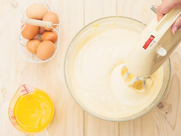 Hand der Dame, die Kuchen unter Verwendung der Handmischmaschine mit Ei und Butter vorbereitet