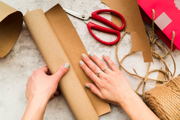 Hand der Frau, die das Handwerk mit braunem Papier auf strukturiertem Hintergrund macht