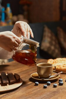 Hand der kellnerin gießt eine tasse tee am tisch des kunden ein, nahaufnahme der glasteekanne mit tee...