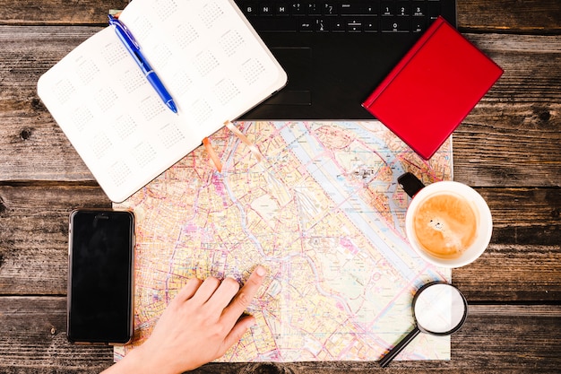 Kostenloses Foto hand der person, die auf standort auf karte mit kaffee und smartphone auf tabelle zeigt