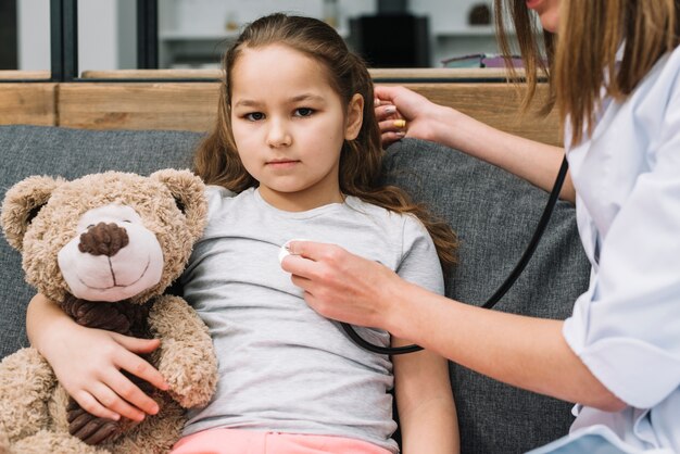 Hand der Ärztin, die das kranke Mädchen hält Teddybären mit Stethoskop überprüft