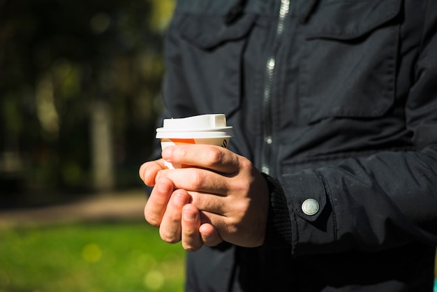 Hand des Mannes, die Wegwerfkaffeetasse hält