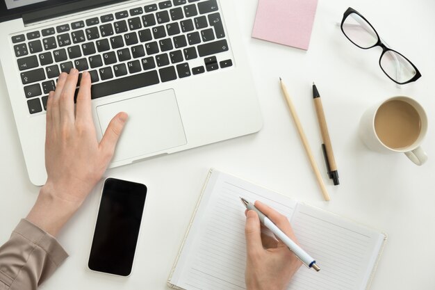 Hand, die an einem Laptop arbeitet, ein anderer hält einen Stift