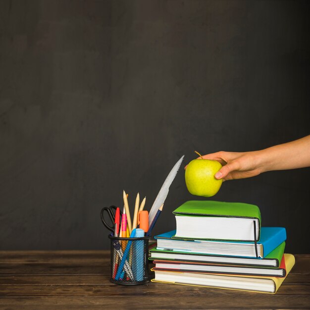 Hand, die Apfel auf Lehrbücher auf Arbeitsplatz setzt