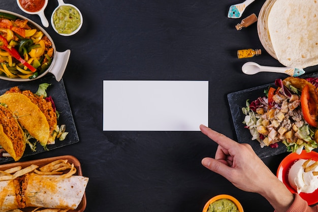Hand, die auf Papier nahe mexikanischem Lebensmittel zeigt