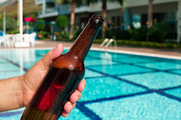 Hand, die Bierflasche am Pool hält