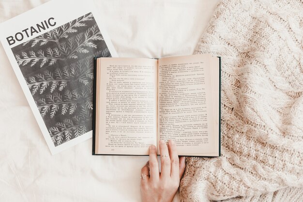 Hand, die Buch auf Plakat und Decke auf Bedsheet berührt