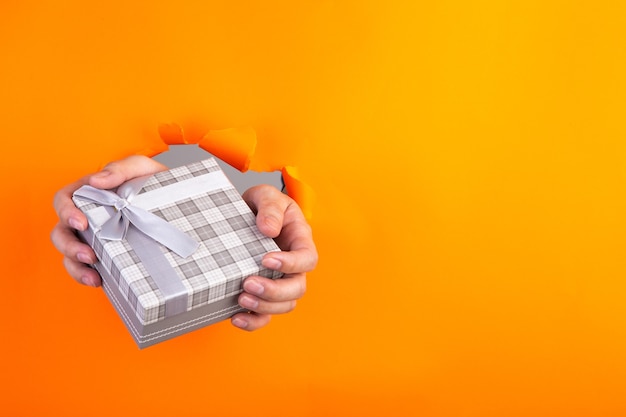 Hand, die ein Geschenk durch ein orange zerrissenes Papier hält