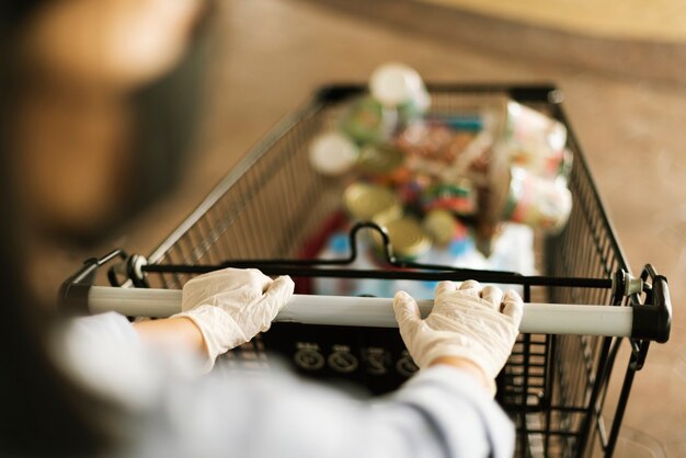 Hand, die einen Latexhandschuh trägt, während Sie einen Einkaufswagen schieben, um eine Kontamination mit Coronavirus zu verhindern