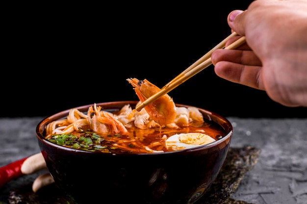 Hand, die Essstäbchen mit Garnelenramen hält