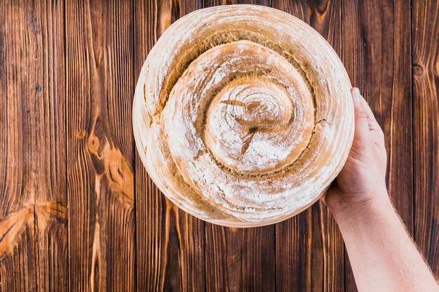 Hand, die frisch gebackenes Strudelbrot auf hölzernem Hintergrund hält