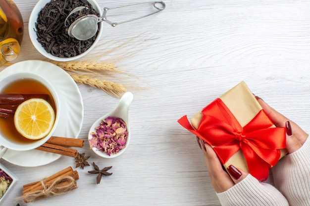 Hand, die Geschenke mit rotem Band und Teepause mit Zimt hält