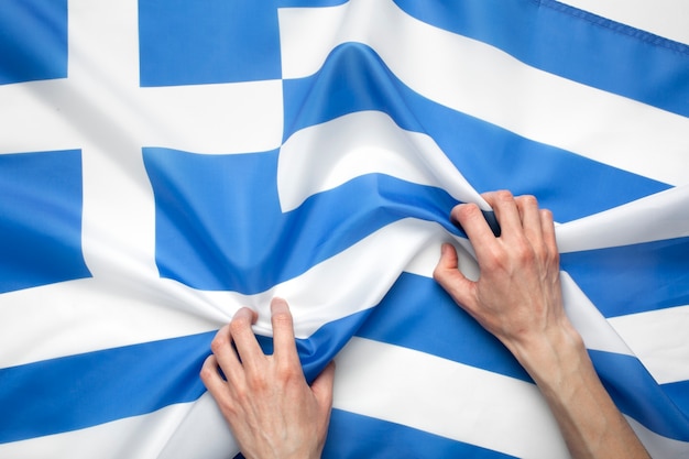 Hand, die griechischen Flaggenstoff hält