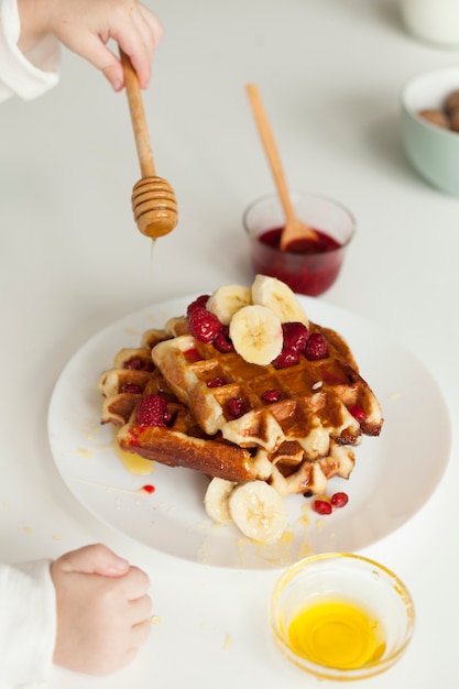 Hand, die Honig auf Waffel setzt