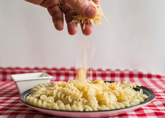 Hand, die Käse auf Teigwaren besprüht