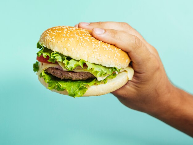 Hand, die köstlichen Burger mit blauem Hintergrund hält