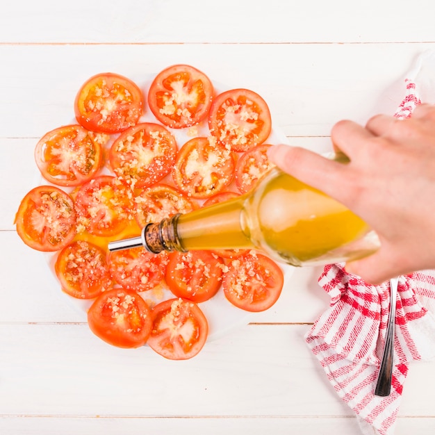 Hand, die Öl auf Tomatenplatte setzt