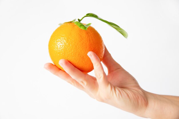 Hand, die Orange mit Blättern durch Finger hält
