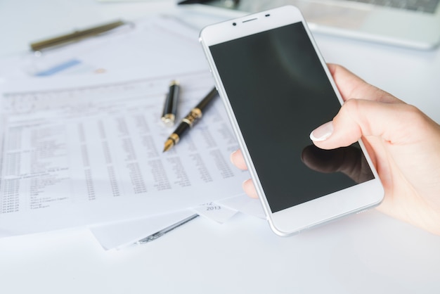 Kostenloses Foto hand, die smartphone am arbeitsplatz hält