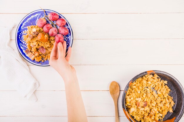 Hand, die Traube auf Platte mit Mahlzeit hält