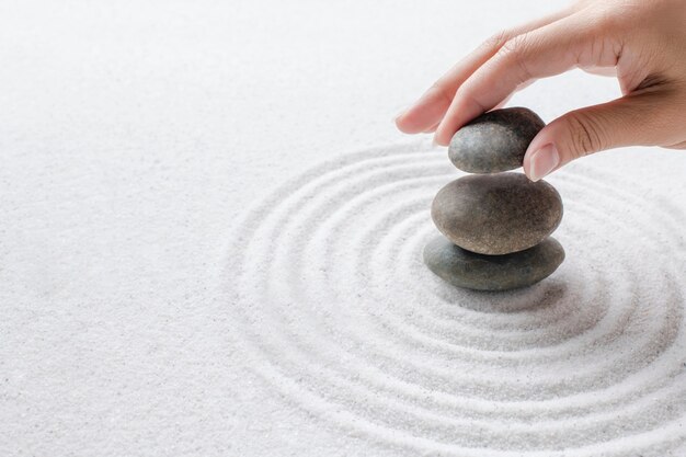 Hand, die Zen-Steine auf dem Sand-Wellness-Hintergrund stapelt