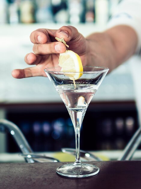 Hand, die Zitrone im alkoholischen Cocktail hinzufügt