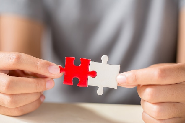 Kostenloses Foto hand, die zwei puzzleteile auf tabellenhintergrund anschließt