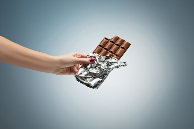 Hand einer Frau, die eine Fliese der Schokolade anhält