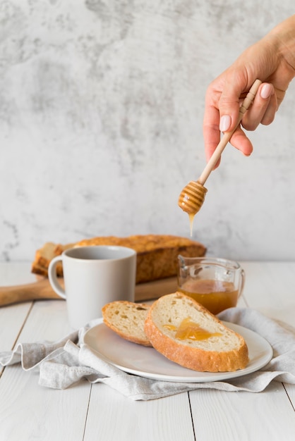 Hand gießt Honig über Brotscheibe