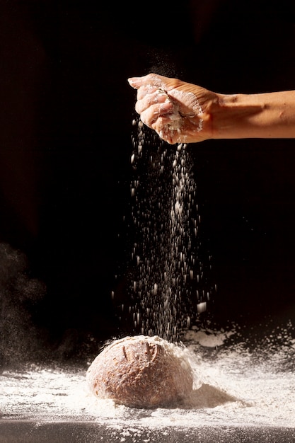 Hand gießt Mehl auf gebackenes Brot