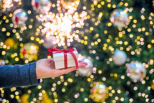 Kostenloses Foto hand hält ein geschenk auf einem glänzenden hintergrund