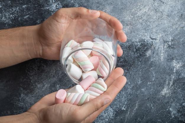 Hand hält ein Glas mit leckeren Marshmallows auf grauem Hintergrund.