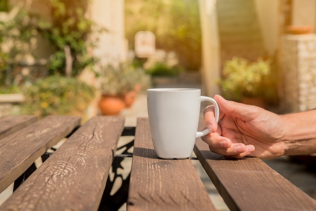Hand hält eine Kaffeetasse. Man trinkt Morgen Kaffee mit einem grünen Hintergrund draußen. Mann Hände halten Tasse Kaffee im Café im Sommer Sommer