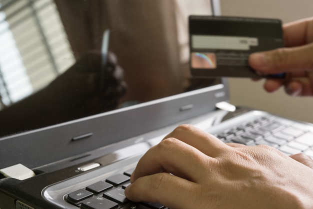 Hand hält eine Kreditkarte und mit Laptop